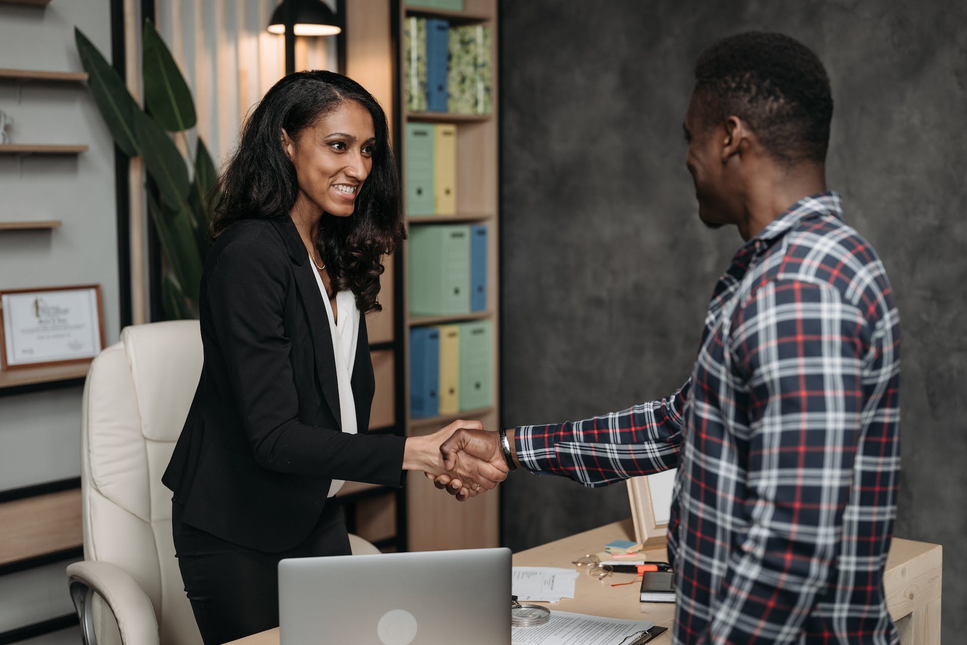 Two individuals shaking hands across a table, symbolising agreement, partnership, and collaboration in a professional setting.