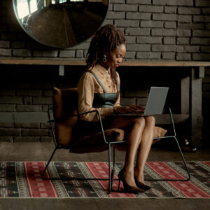 A focused individual participating in a Master Social Media Coaching Programme, attentively working on a laptop in a chic, rustic room with a brick wall background.