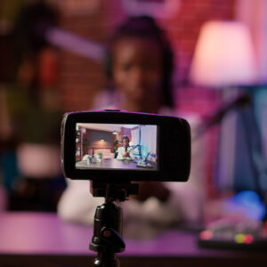 A woman is actively participating in a "TikTok for Business and Influencers Workshop," recording herself with a smartphone on a tripod. The focus of the image is on the phone's screen, showing her confident expression. The background is softly illuminated with warm, ambient lighting, indicating a cozy indoor setting that's likely her personal workspace.