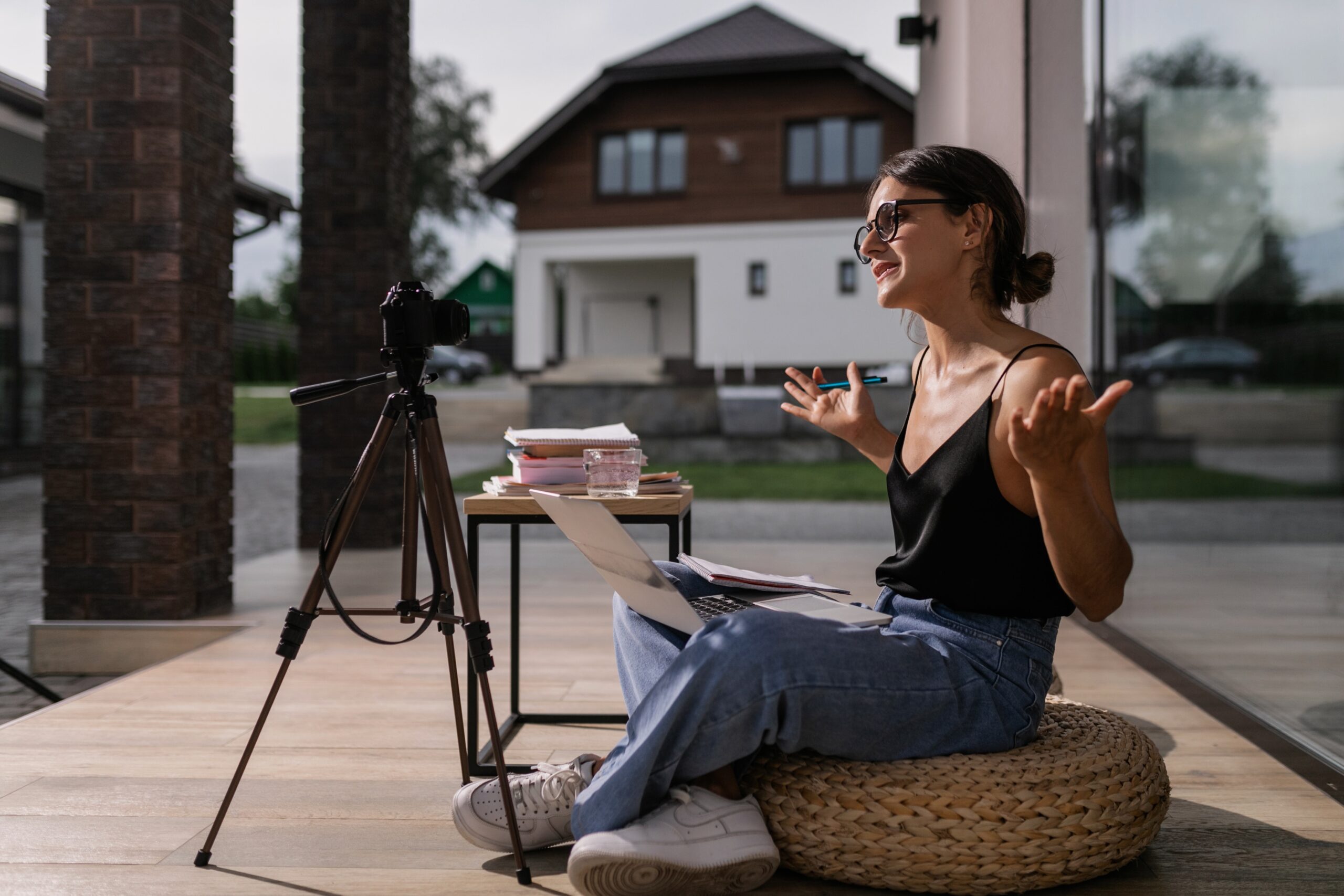 An enthusiastic content creator engaging with her audience through a live video session outdoors, with a professional camera set up on a tripod and a laptop on a small table, embodying the spirit of DIY personal brand content creation.