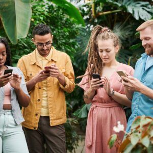 A diverse group of four people in a lush greenhouse, each focused intently on their smartphones. They stand amid vibrant green foliage, suggesting a relaxed yet engaging atmosphere of learning and connectivity. This image evokes a sense of community and the shared pursuit of knowledge, embodying the collaborative spirit of the "Instagram Branding Seminar".