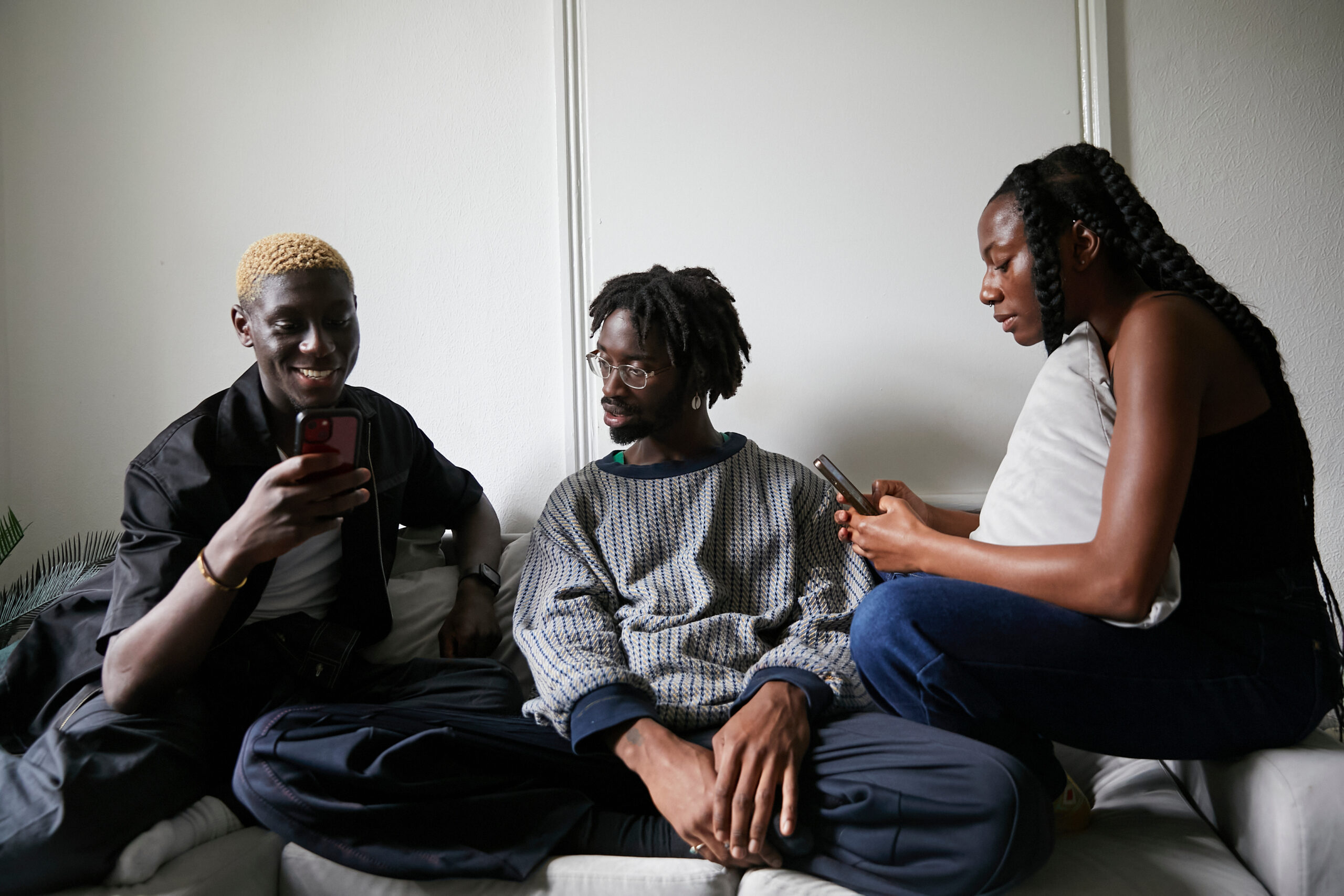 Stylish friendship group of three using their phones whilst sitting on a sofa, symbolising the collaborative effort to unlock the Instagram growth secret.