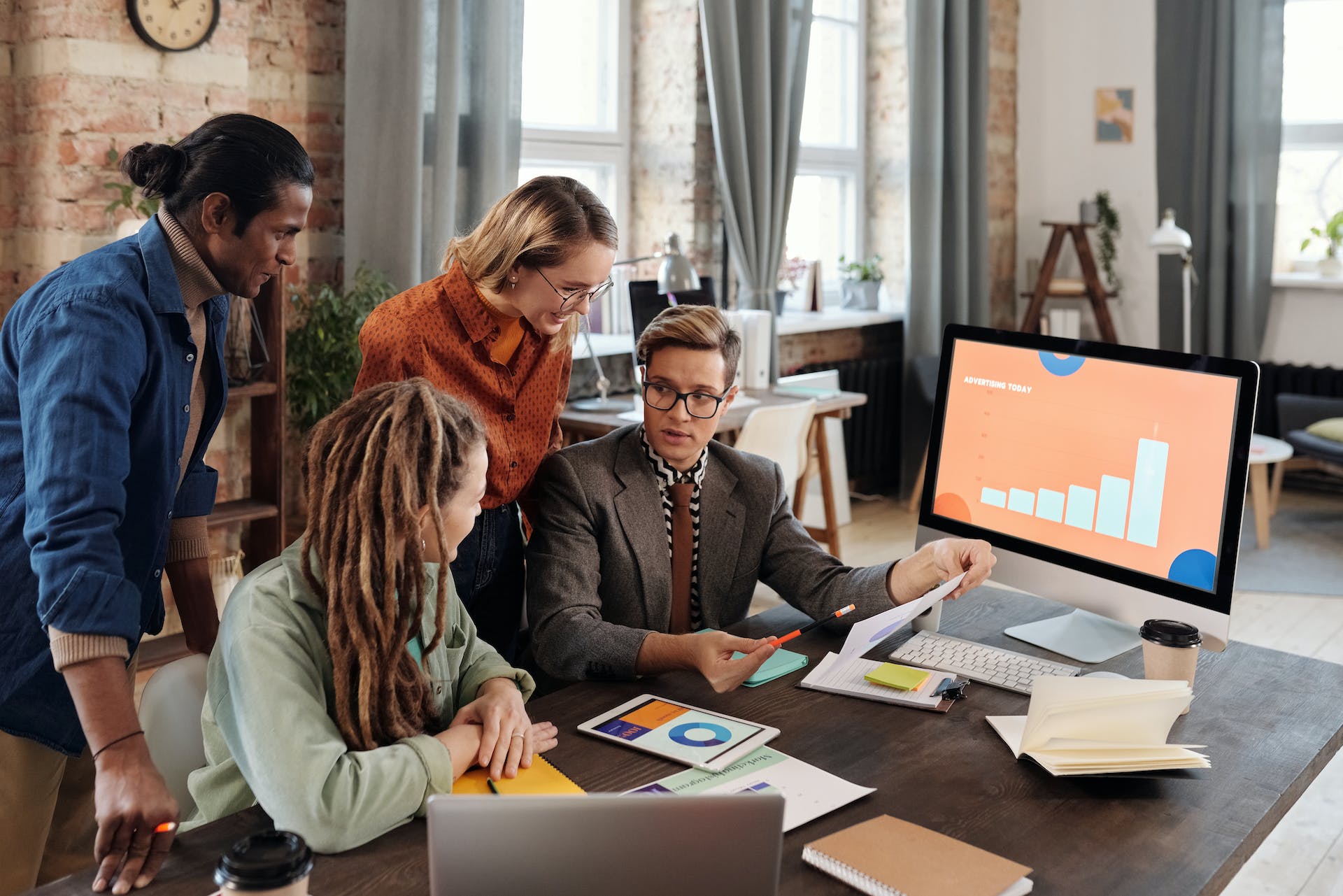 Four professionals engaged in brand building growth strategy, analyzing graphs on a computer monitor in a well-lit, modern workspace.