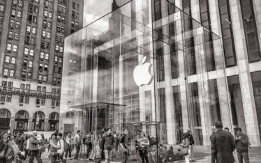 Customers gather around the bustling entrance of an iconic glass-walled Apple Store, symbolising the iPhone luxury trend in modern technology retail