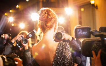 Female celebrity facing a crowd of reporters and fans at a red carpet event, with flash photography capturing the moment, illustrating the concept of Viral Marketing Strategies through public attention and media presence.