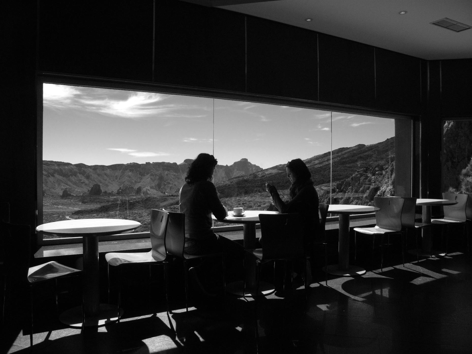 Two individuals engaging in a heartfelt conversation by a large window overlooking a serene mountain landscape, embodying the concept of embracing life.