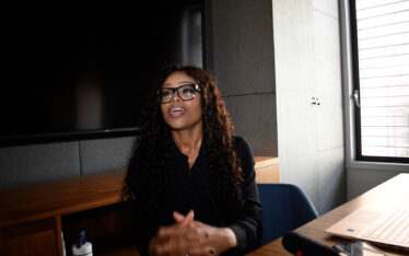 Bess Obarotimi seated at a conference table in an office setting, engaged in conversation and using hand gestures, embodying the theme of rediscovering ambition and vision