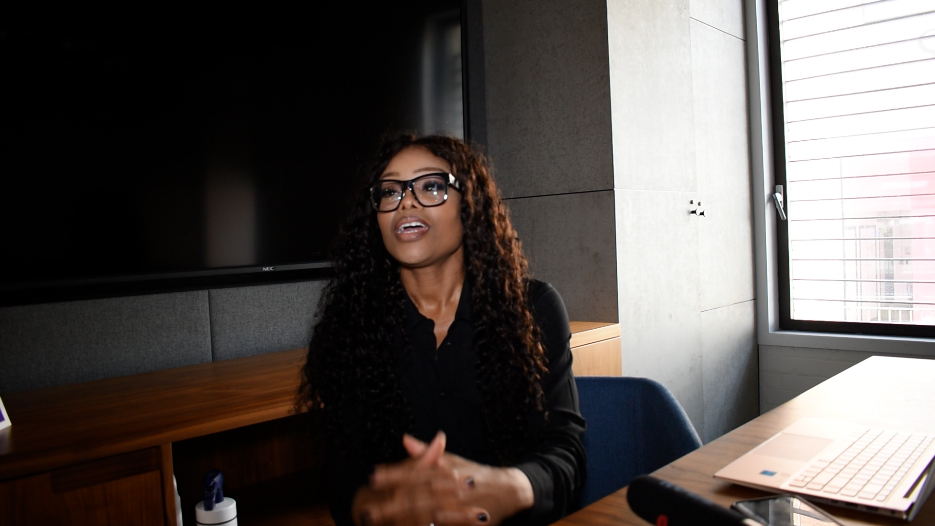 Bess Obarotimi seated at a conference table in an office setting, engaged in conversation and using hand gestures, embodying the theme of rediscovering ambition and vision