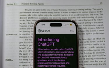 Smartphone with an introduction screen for ChatGPT, placed over a textbook discussing problem-solving agents, emphasizing the keyword 'ChatGPT social media limitations' by contrasting AI dialogue capabilities with personal storytelling needs in social media branding."