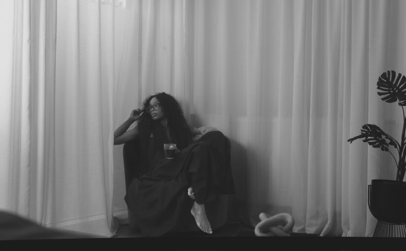 Bess Obarotimi sitting peacefully by white curtains, holding a drink, reflecting — promotional image for the I AM Success book.