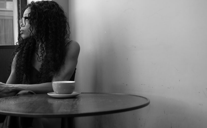 Woman seated at a table in a café, looking out of a window, used to accompany an article on decision-making authority and responsibility.