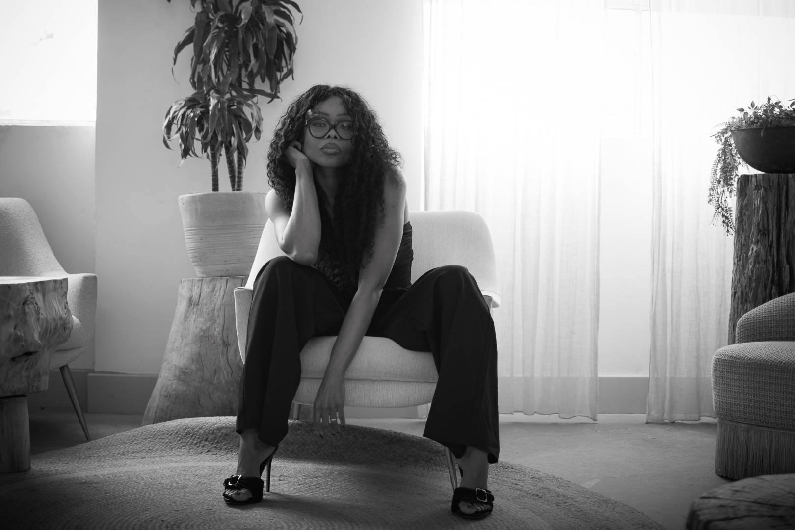 Black-and-white portrait of a woman seated in a minimalist room, looking thoughtful and composed, representing reflection, judgement and decision quality.